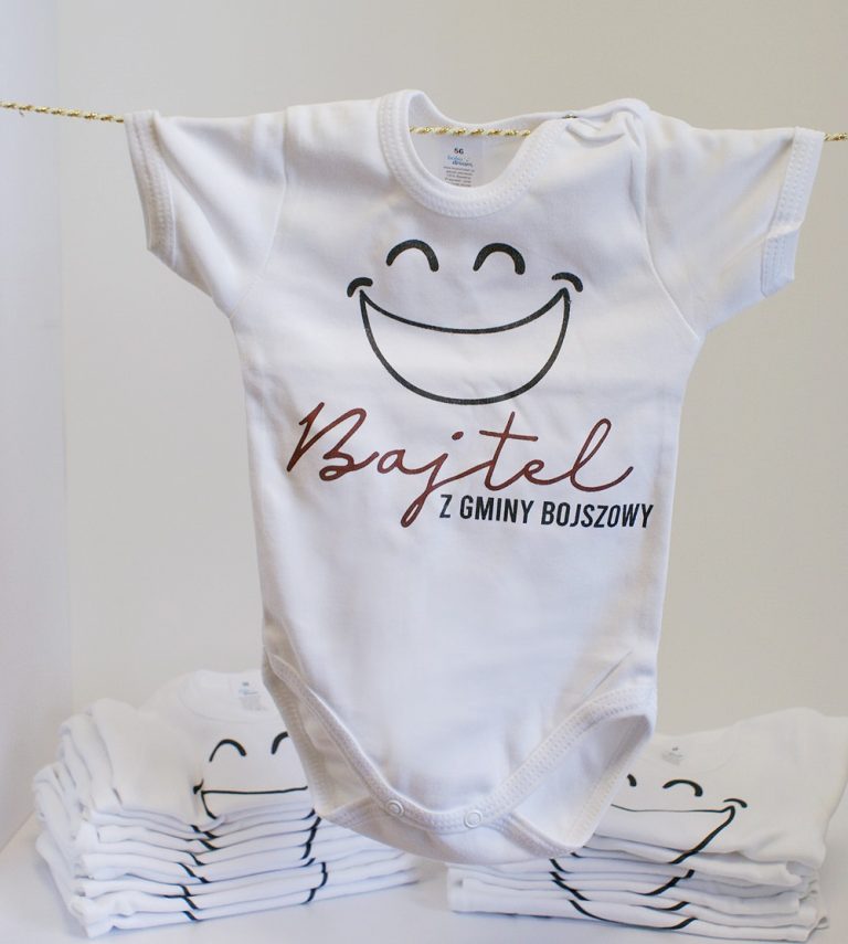 Białe body niemowlęce z logiem akcji Bajtel z gminy Bojszowy. Nad logiem uśmiechnięta buźka
